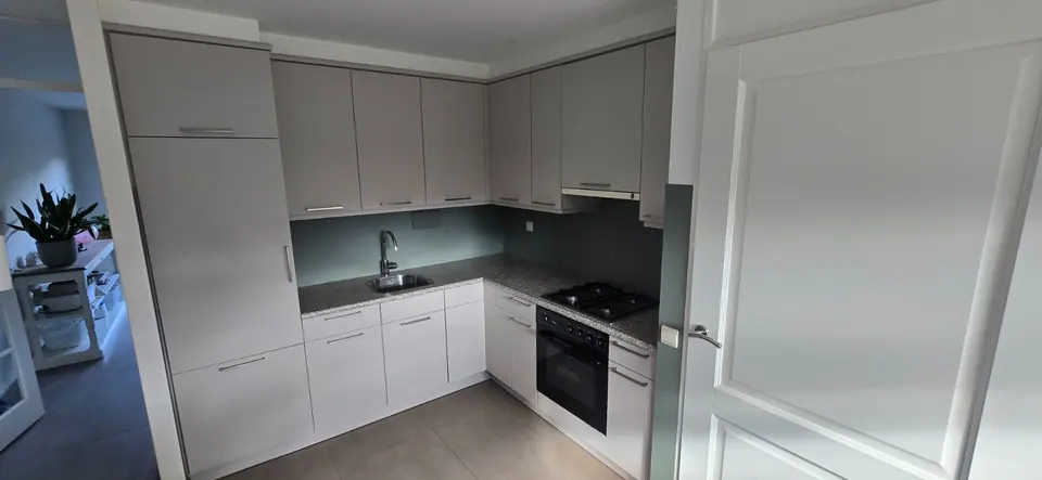 Na de renovatie: dezelfde keuken met lichtgrijze fronten en een grijsgroene achterwand